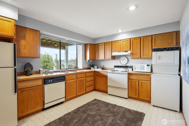 kitchen with under cabinet range hood, light floors, white appliances, and stacked washer / drying machine