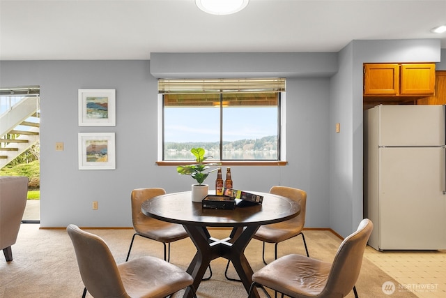 dining room featuring baseboards, light colored carpet, and stairs