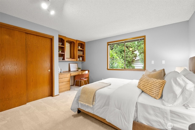 bedroom with light colored carpet, built in desk, a closet, and a textured ceiling