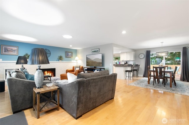 living room with recessed lighting, a brick fireplace, and light wood-type flooring