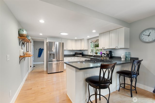 kitchen with light wood finished floors, a peninsula, white cabinets, appliances with stainless steel finishes, and dark countertops