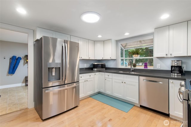 kitchen featuring dark countertops, stainless steel appliances, light wood-style floors, white cabinetry, and a sink