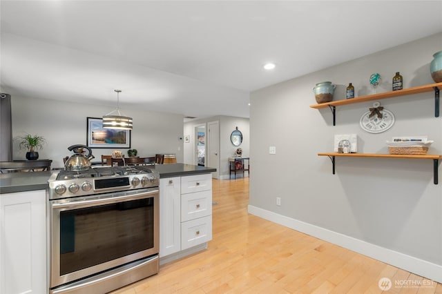 kitchen featuring open shelves, stainless steel range with gas cooktop, dark countertops, and white cabinetry