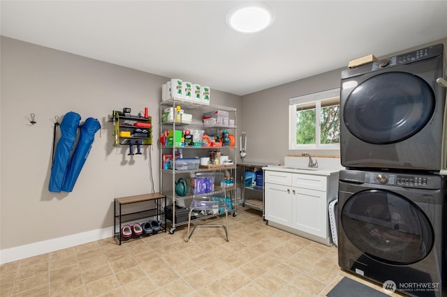 clothes washing area with a sink, baseboards, cabinet space, and stacked washer and dryer