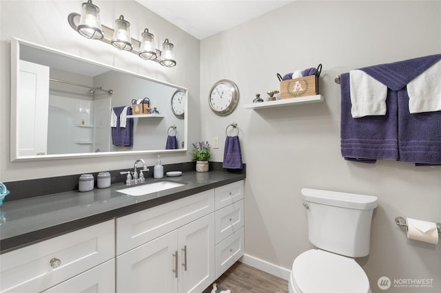 bathroom with baseboards, walk in shower, toilet, wood finished floors, and vanity