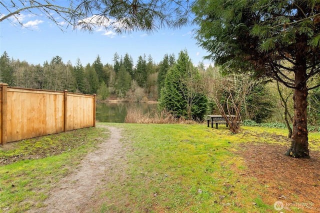 view of yard with fence, a water view, and a view of trees