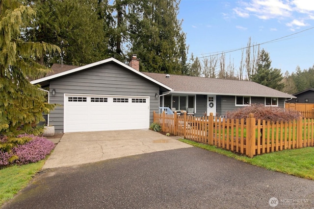 ranch-style home with a shingled roof, a fenced front yard, concrete driveway, a chimney, and an attached garage