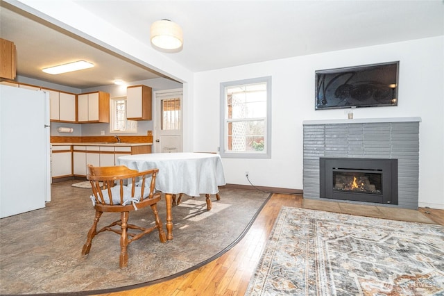 dining room featuring baseboards, plenty of natural light, a brick fireplace, and light wood finished floors