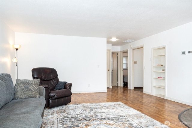 living room with built in features, visible vents, baseboards, and wood finished floors