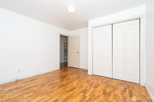 unfurnished bedroom with a closet, baseboards, and light wood-style floors