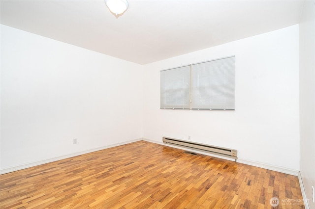 empty room with a baseboard heating unit, baseboards, and light wood finished floors