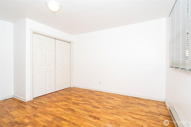 unfurnished bedroom with a closet, baseboards, baseboard heating, and light wood finished floors