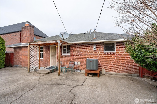 back of property featuring fence, a shingled roof, central air condition unit, a patio area, and brick siding