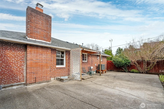 rear view of house with brick siding, fence, central AC, a chimney, and a patio