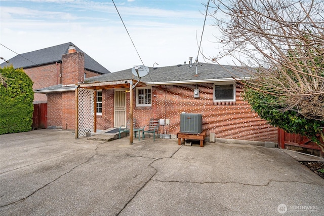 rear view of property with brick siding, a patio area, and a shingled roof