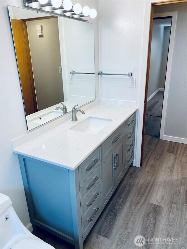 bathroom with toilet, vanity, baseboards, and wood finished floors