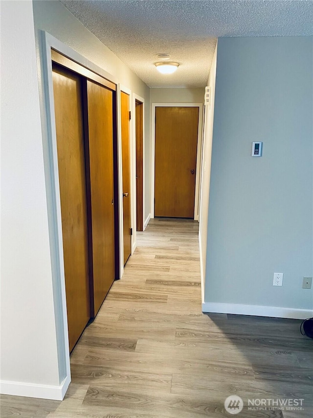 hall featuring light wood-style flooring, a textured ceiling, and baseboards