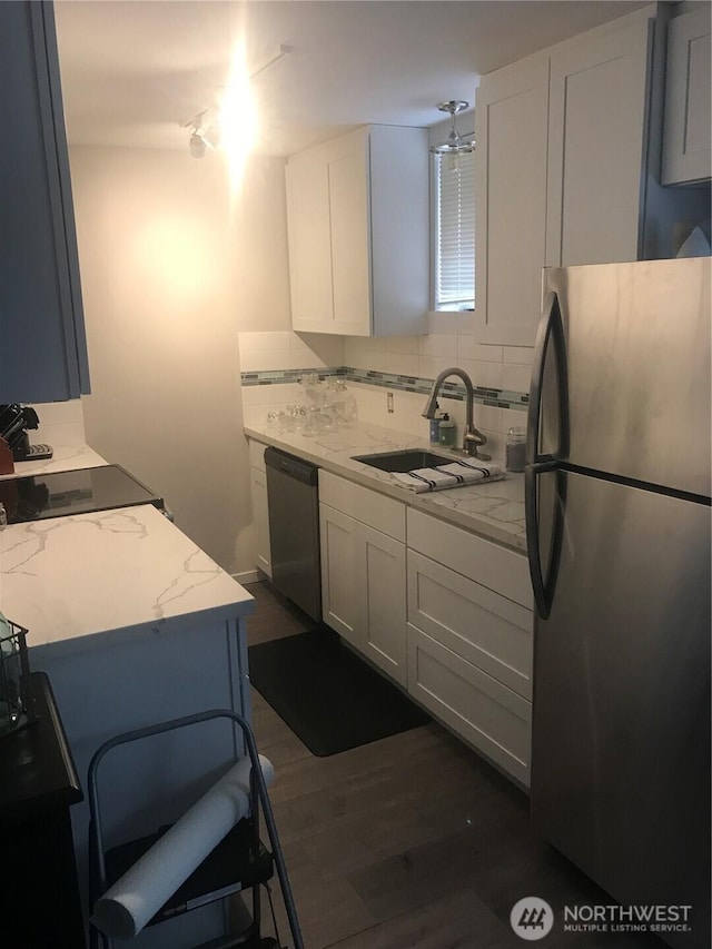 kitchen with tasteful backsplash, light stone countertops, white cabinets, stainless steel appliances, and a sink