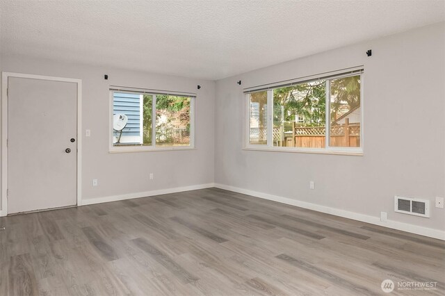 spare room with a textured ceiling, wood finished floors, and baseboards