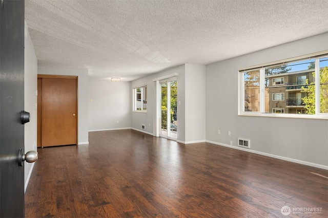 unfurnished room with a textured ceiling, plenty of natural light, wood finished floors, and baseboards