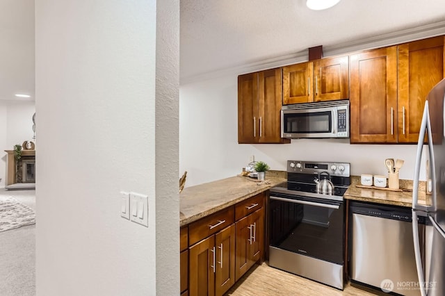 kitchen featuring light stone counters, appliances with stainless steel finishes, a glass covered fireplace, and crown molding