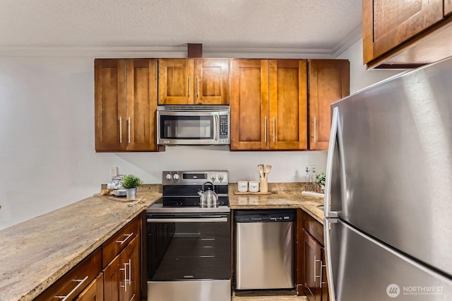 kitchen featuring brown cabinets, a textured ceiling, stainless steel appliances, crown molding, and light stone countertops