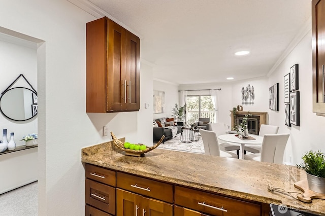 kitchen with light stone counters, brown cabinetry, open floor plan, and ornamental molding