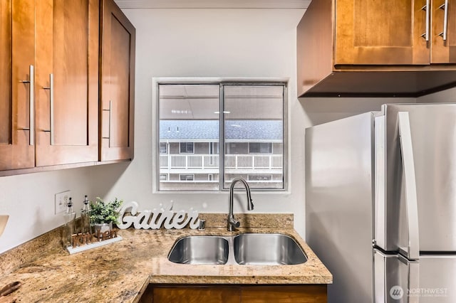 kitchen with a sink, light stone countertops, brown cabinetry, and freestanding refrigerator