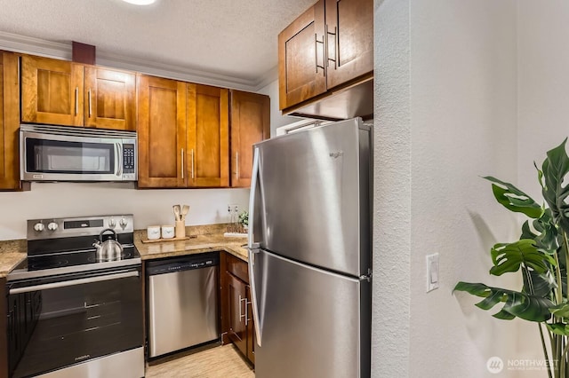 kitchen featuring light stone counters, stainless steel appliances, a textured ceiling, crown molding, and brown cabinets