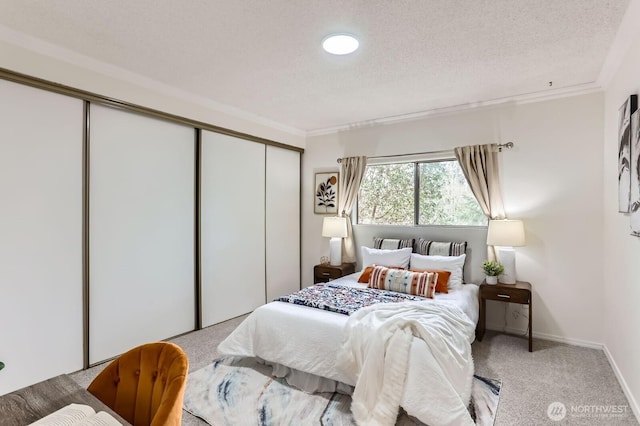 carpeted bedroom with a closet, a textured ceiling, baseboards, and ornamental molding