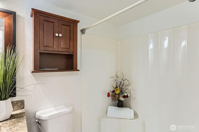 bathroom featuring toilet and a textured wall