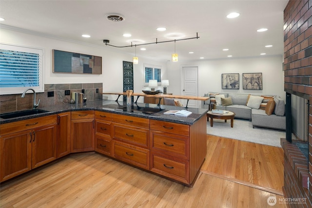 kitchen with light wood-type flooring, a sink, dark stone counters, a peninsula, and brown cabinetry