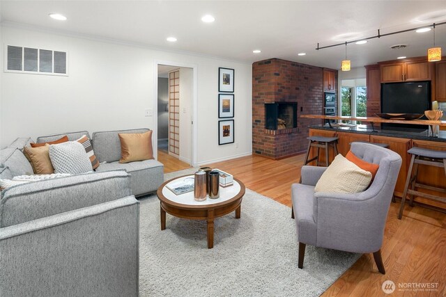 living room featuring visible vents, ornamental molding, recessed lighting, a fireplace, and light wood finished floors