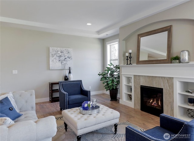 living room featuring a tiled fireplace, baseboards, and wood finished floors