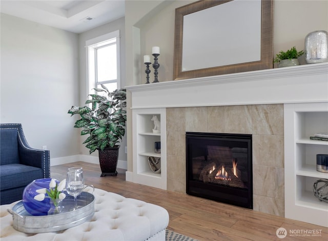 living room with built in features, wood finished floors, baseboards, and a tile fireplace