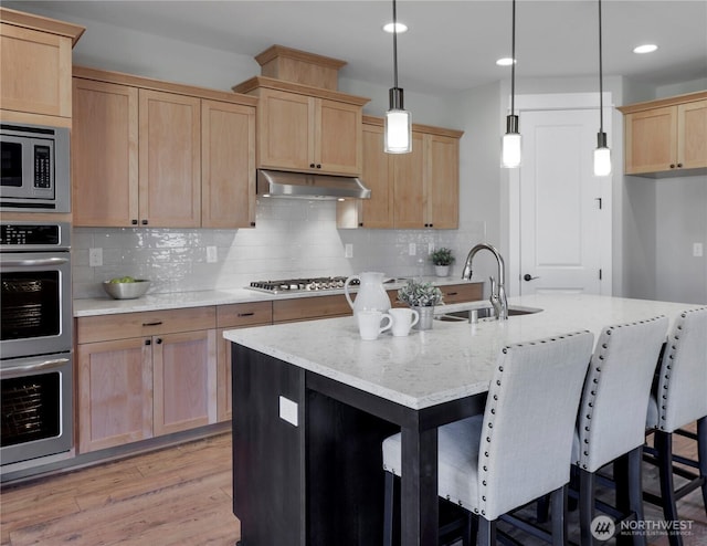 kitchen featuring light brown cabinets, under cabinet range hood, a sink, light wood-style floors, and appliances with stainless steel finishes