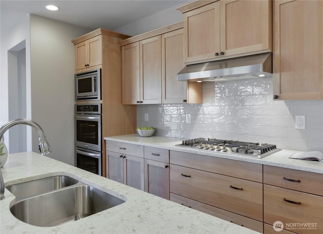 kitchen with light brown cabinetry, under cabinet range hood, a sink, appliances with stainless steel finishes, and decorative backsplash