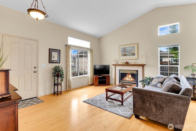 living area with wood finished floors, plenty of natural light, a glass covered fireplace, and vaulted ceiling