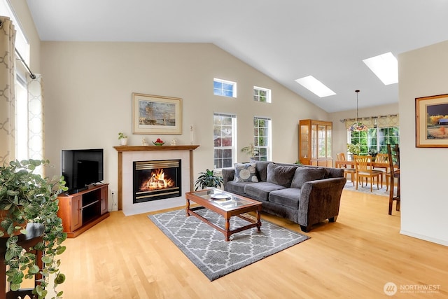 living area featuring light wood finished floors, high vaulted ceiling, a tile fireplace, and a skylight