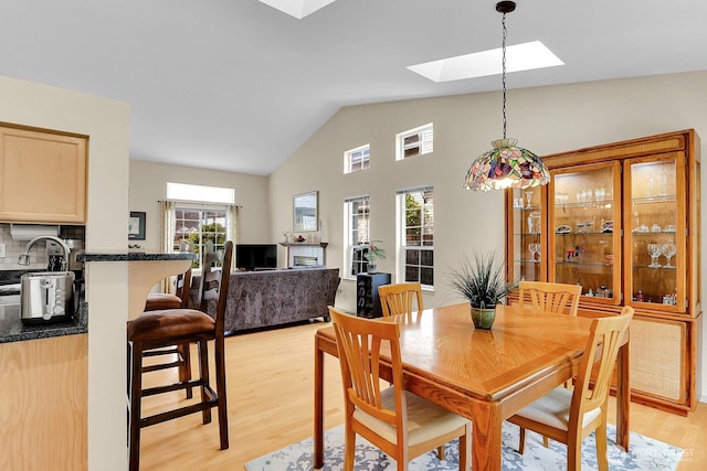 dining area with vaulted ceiling with skylight and light wood-style floors