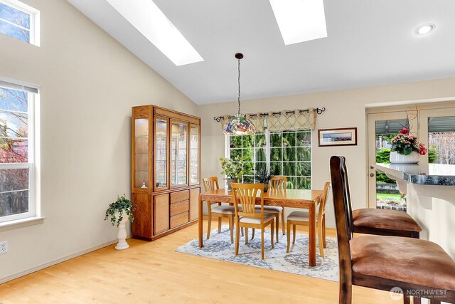 dining room with plenty of natural light, light wood-style flooring, a skylight, and high vaulted ceiling