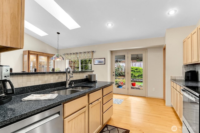 kitchen with light wood finished floors, vaulted ceiling with skylight, light brown cabinetry, a sink, and appliances with stainless steel finishes