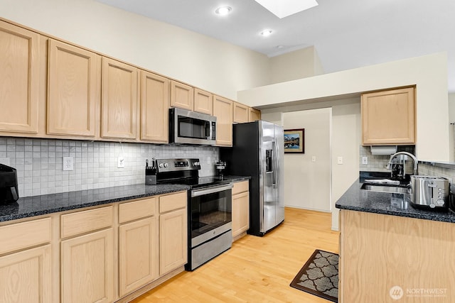 kitchen with light brown cabinetry, a skylight, light wood-style floors, stainless steel appliances, and a sink