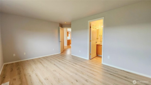 unfurnished bedroom featuring connected bathroom, light wood-type flooring, and baseboards