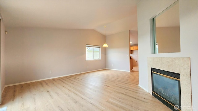 unfurnished living room with a tile fireplace, baseboards, light wood-style floors, and vaulted ceiling