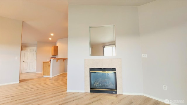 unfurnished living room featuring baseboards, light wood-style flooring, and a tiled fireplace