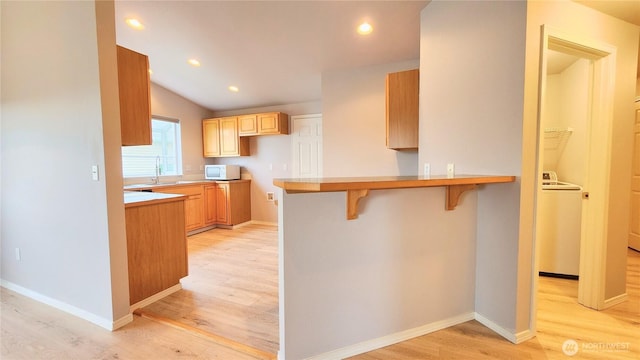 kitchen featuring a breakfast bar area, white microwave, washer / dryer, light wood-style flooring, and recessed lighting