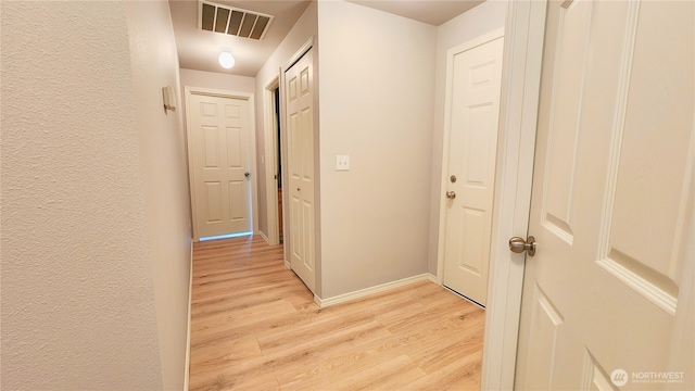 corridor featuring light wood-type flooring, visible vents, baseboards, and a textured wall