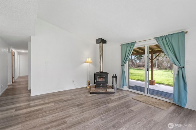 unfurnished living room with a textured ceiling, a wood stove, baseboards, and wood finished floors