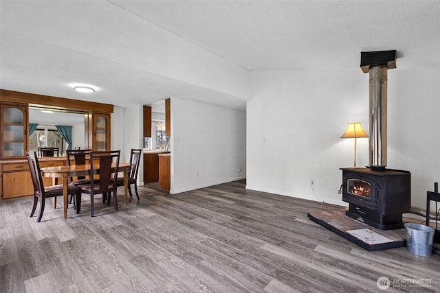 dining room featuring baseboards, a textured ceiling, wood finished floors, and a wood stove